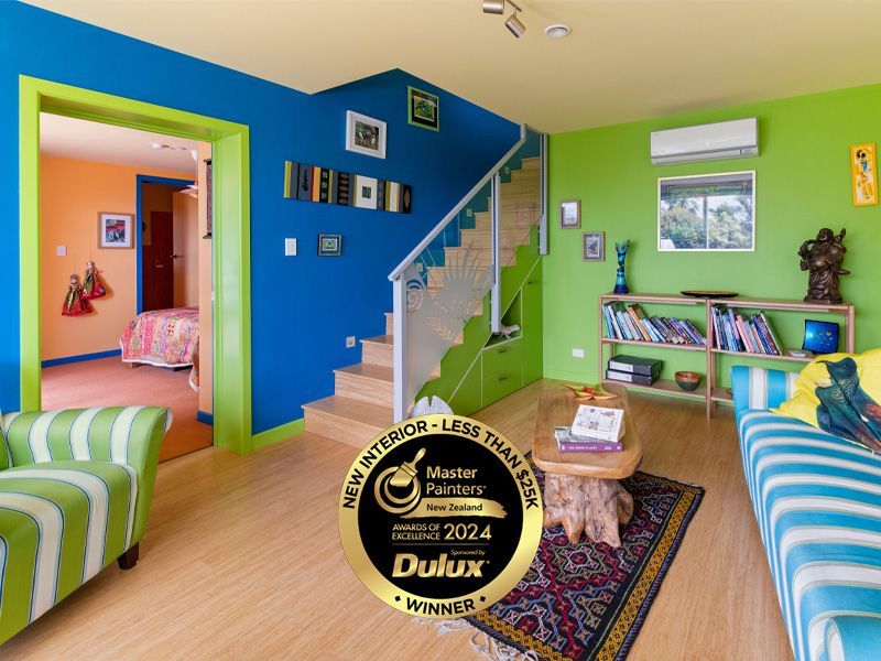 Vibrant room with blue, green, and orange walls. Awards logo on the floor. Staircase and furniture are visible.