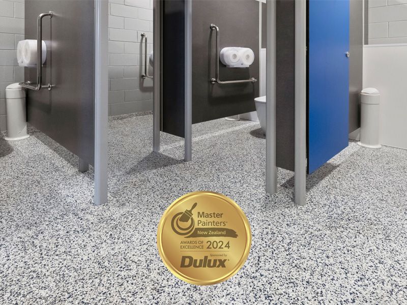 Public restroom with speckled flooring, stalls, grab bars, and a 