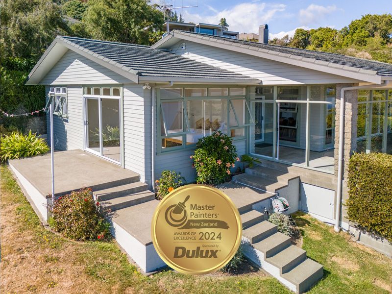 Exterior view of a light blue house with a small porch, steps, and a Master Painters award.