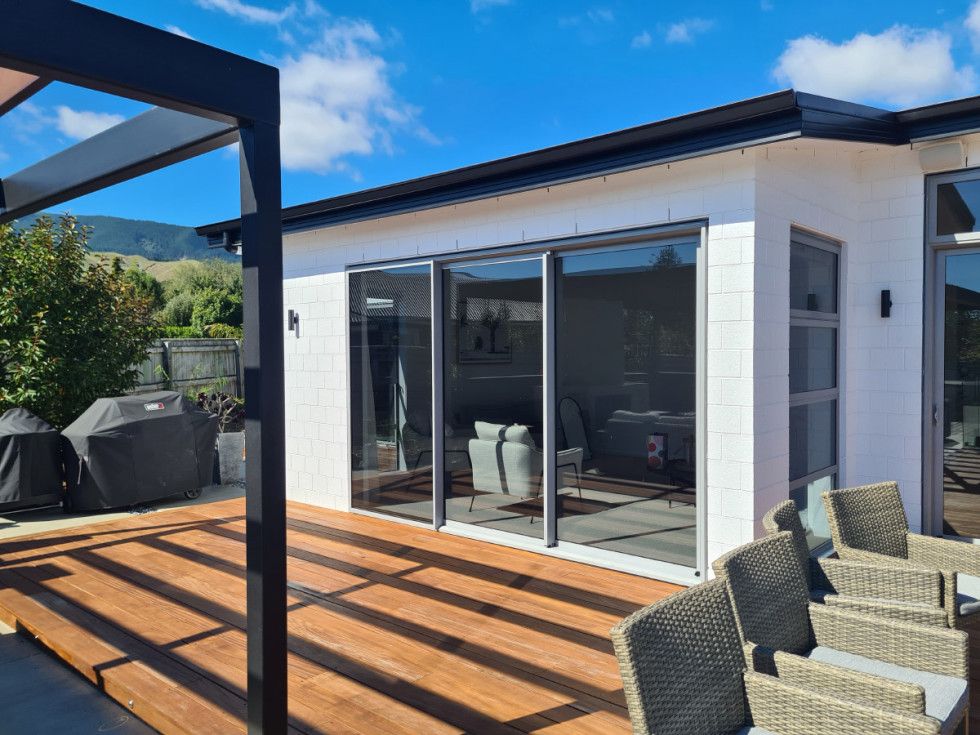 Wooden deck with outdoor seating next to a white building with large glass doors.