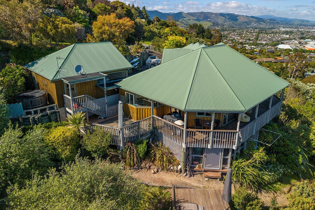 Two hillside homes with green roofs and wooden decks, surrounded by trees.
