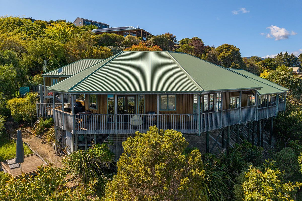 Elevated wooden house with green roof, surrounded by trees on a hillside.