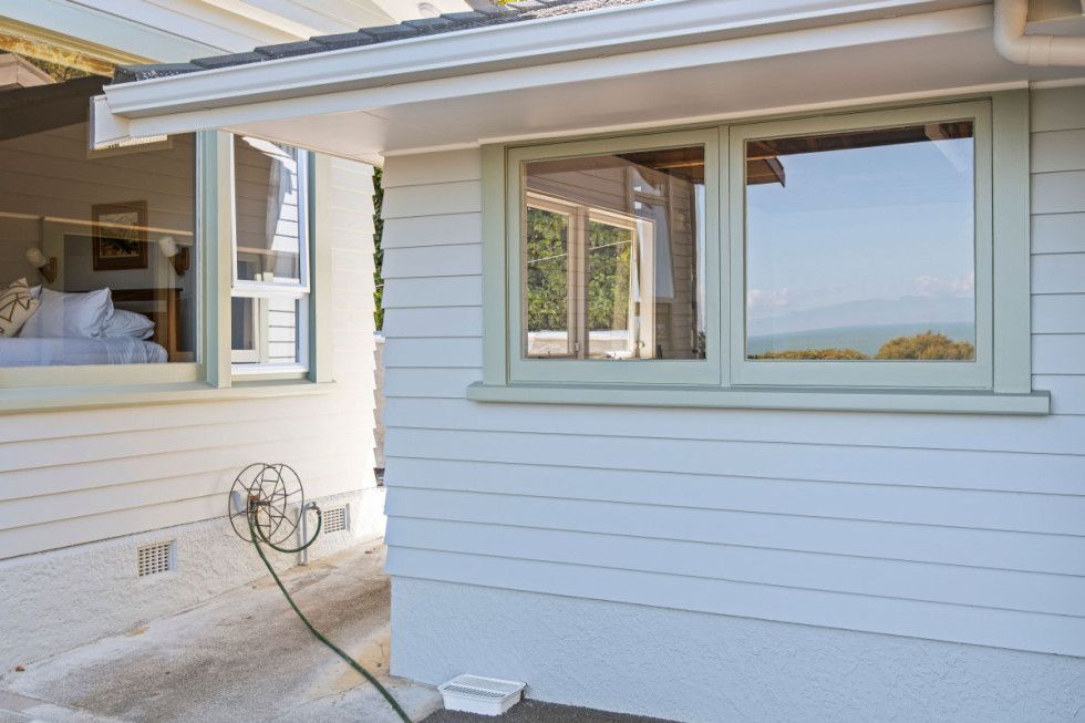 White building exterior with green-framed windows, reflecting an outdoor view, hose coiled near a wall.