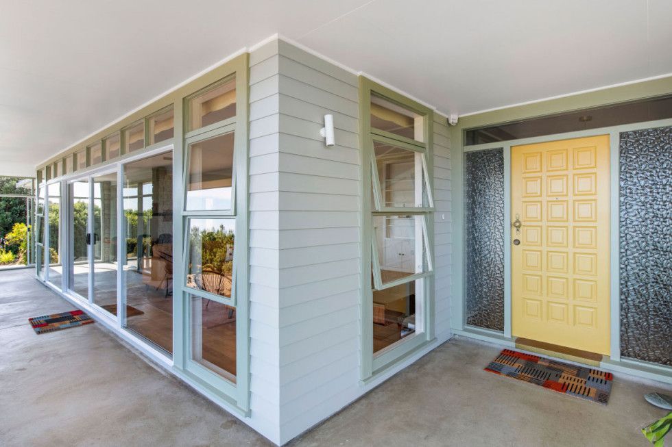 Exterior of a house with large windows, light green siding, and a yellow front door.