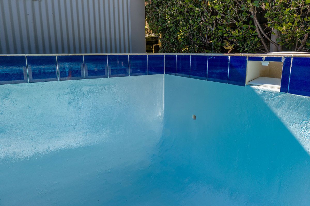 Blue-tiled pool with light blue water and a white wall, under a sunny sky.