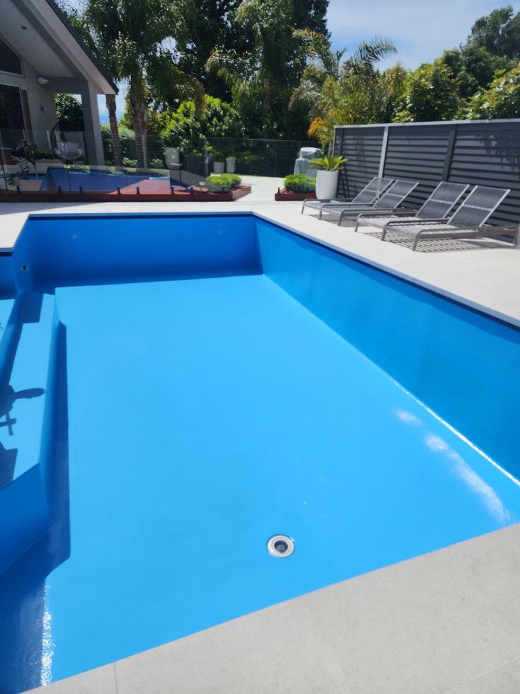 Rectangular pool with blue tile border, surrounded by rose bushes and a green hedge.