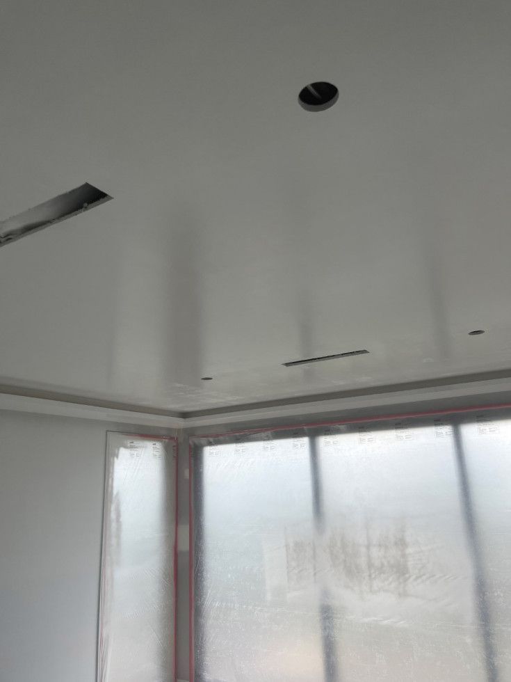 Ceiling with recessed lighting, air vents, and window in a room under construction.