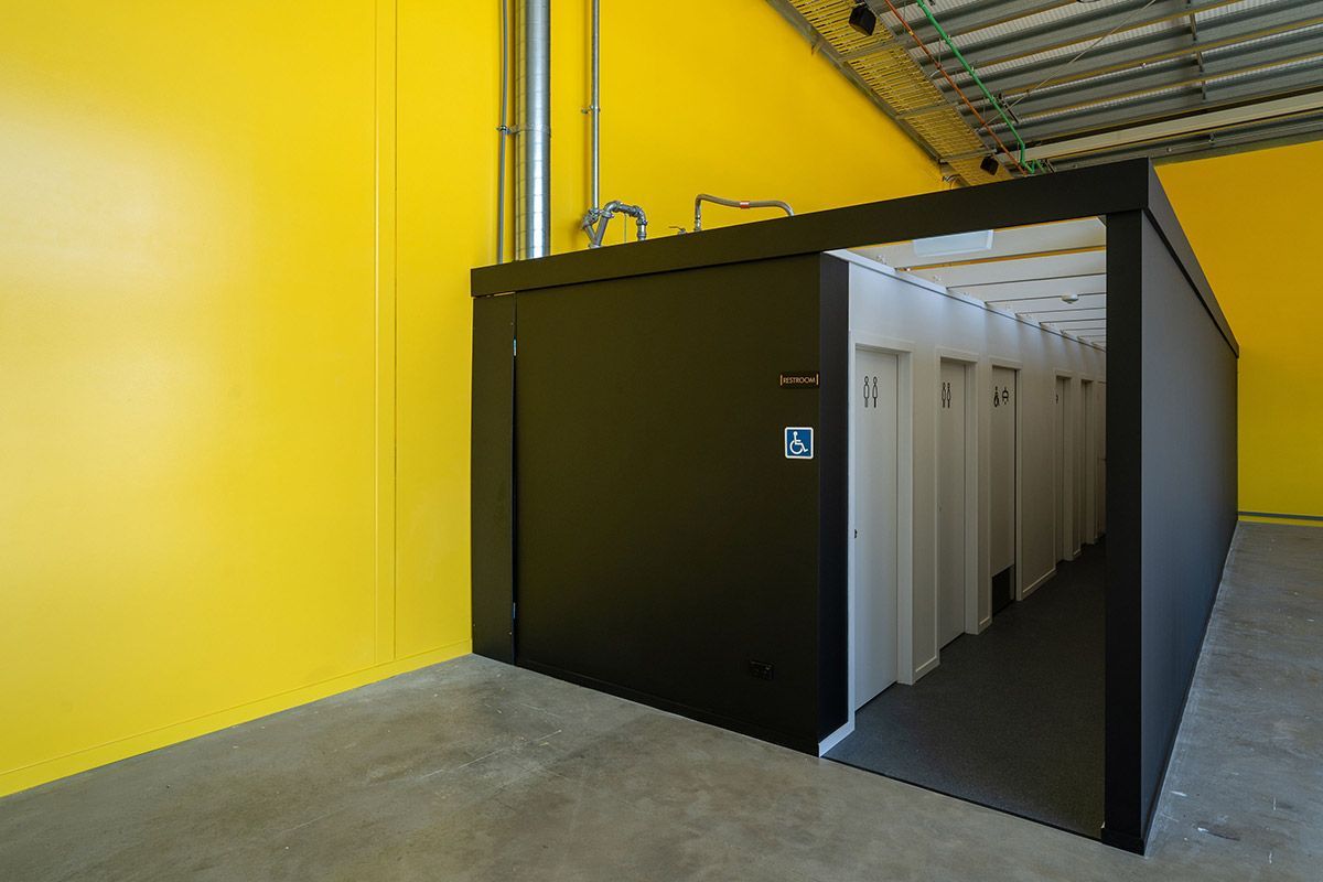 White two-story house with black roof and multiple windows, set on a green grassy hill under a cloudy sky.