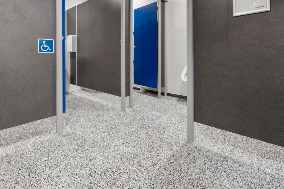 Interior of a public restroom with accessible stall, gray walls, speckled floor, blue stall door.