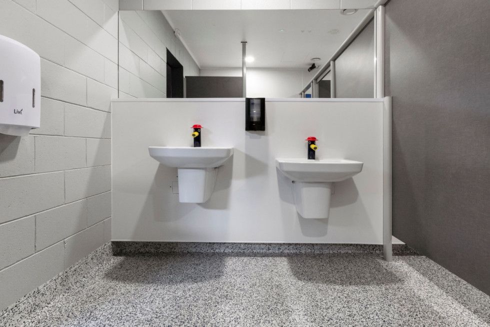 Public bathroom with two sinks, paper towel dispenser, mirror, and gray speckled floor.