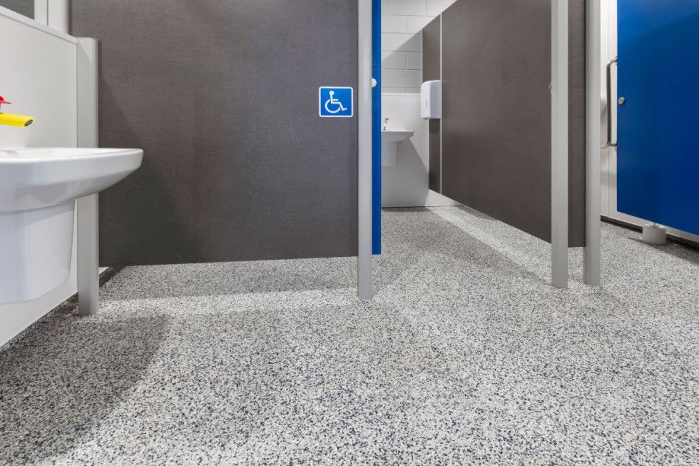 Public restroom with accessible stall featuring gray speckled floor, gray walls, and blue stall door.