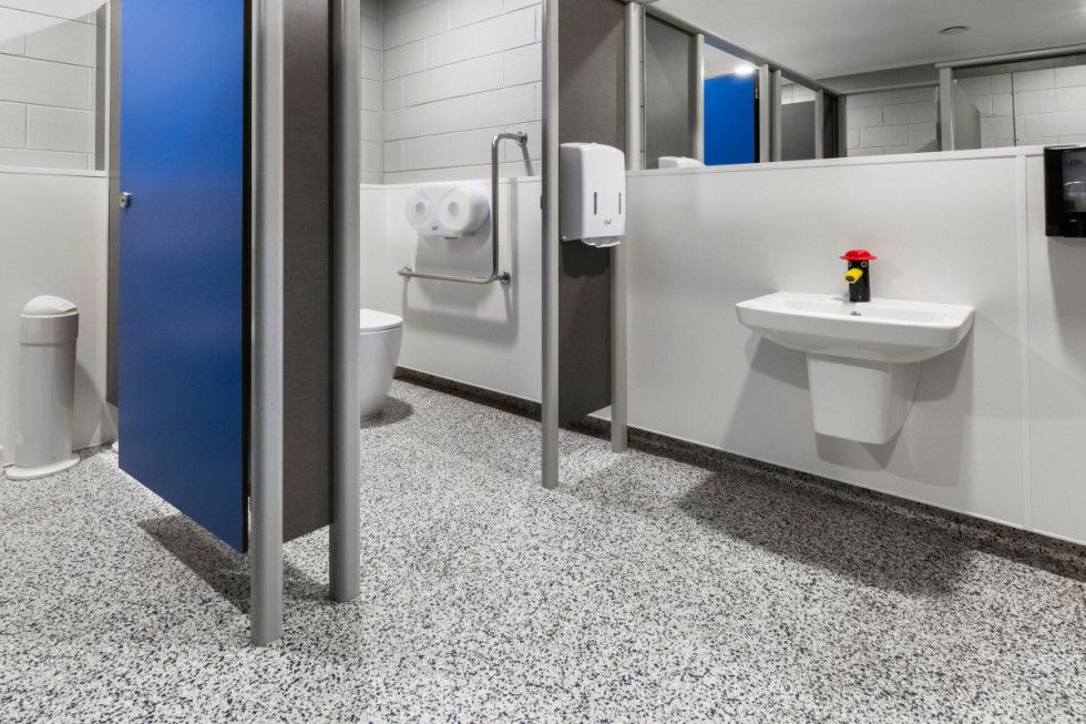 Public restroom with blue stall door, accessible sink, hand dryer, and patterned floor.