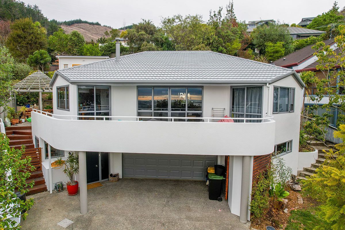 White house with curved balcony, garage, and trees on a hillside.