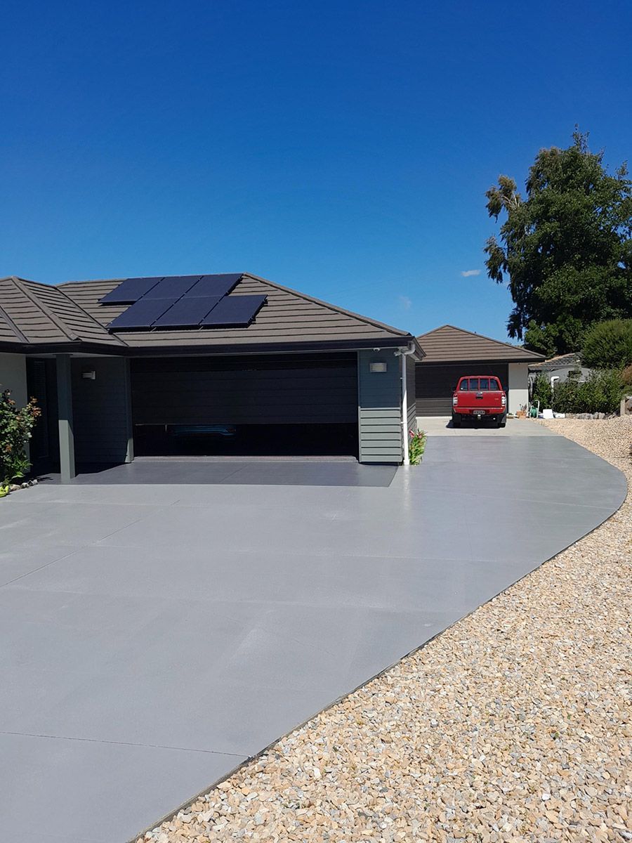 House with gray driveway, open garage, and red truck parked outside, solar panels on the roof.