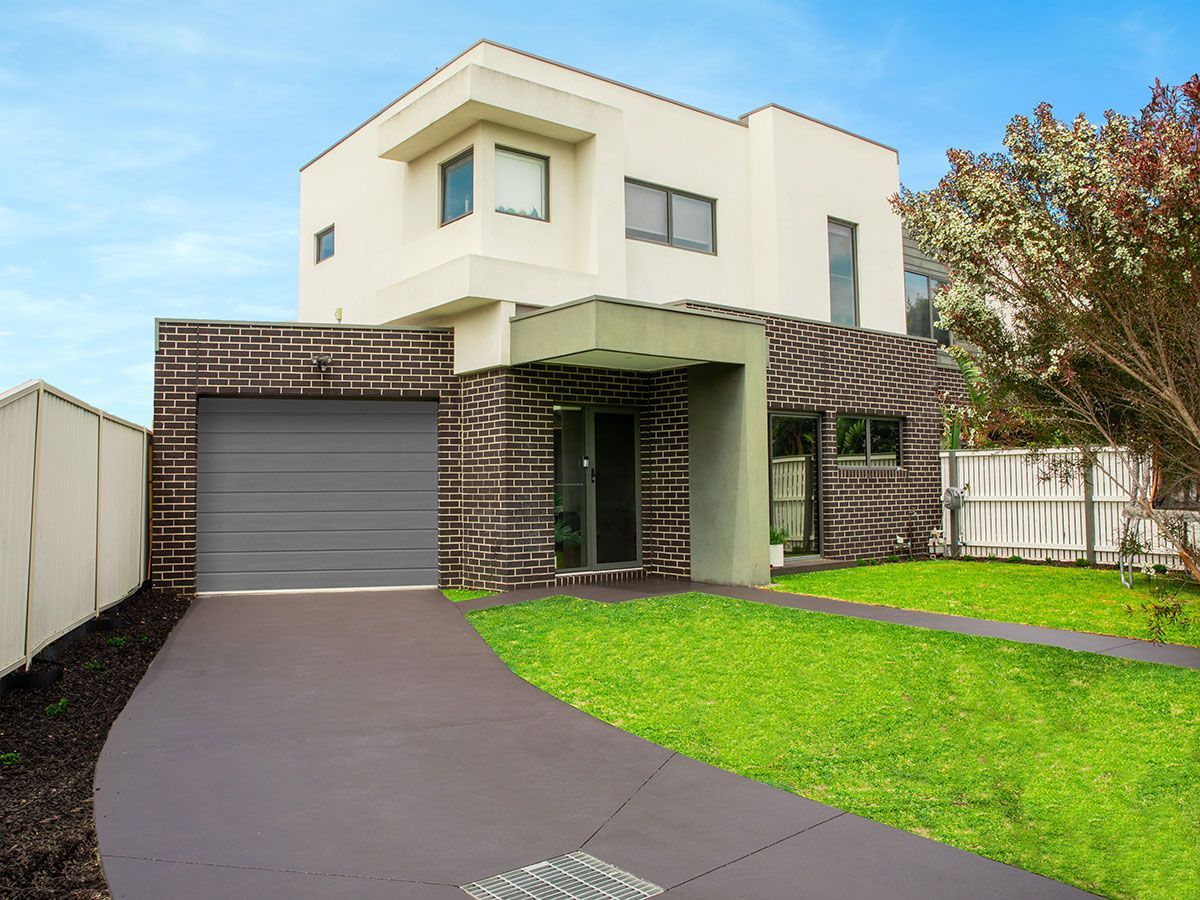Modern two-story house with attached garage, dark brick accent wall, green lawn, driveway.