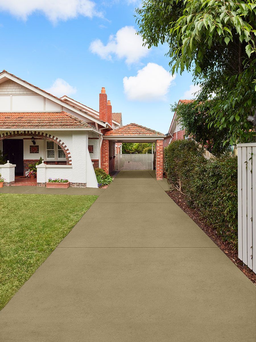Driveway leading to a brick carport and house under a blue sky, with greenery alongside.