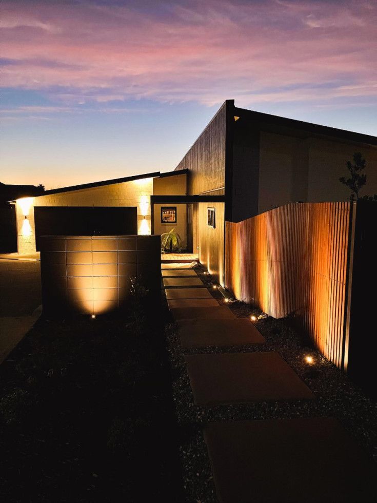 Modern house exterior illuminated by pathway and fence lights at dusk. Pink and blue sky.