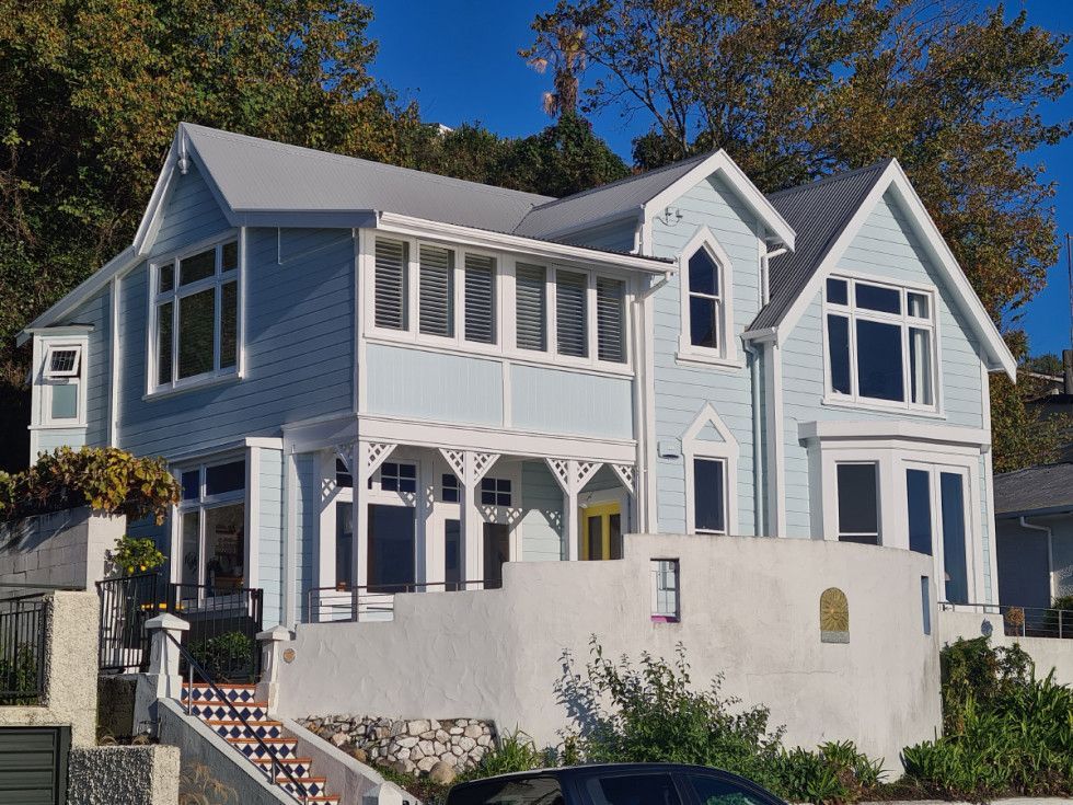 Two-story blue house with white trim, set on a hillside.