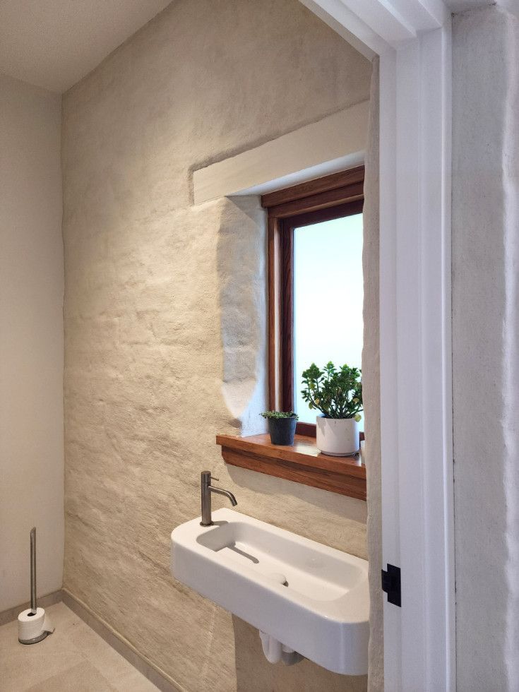 Small bathroom with textured beige walls, a white sink, and a window with plants on the sill.