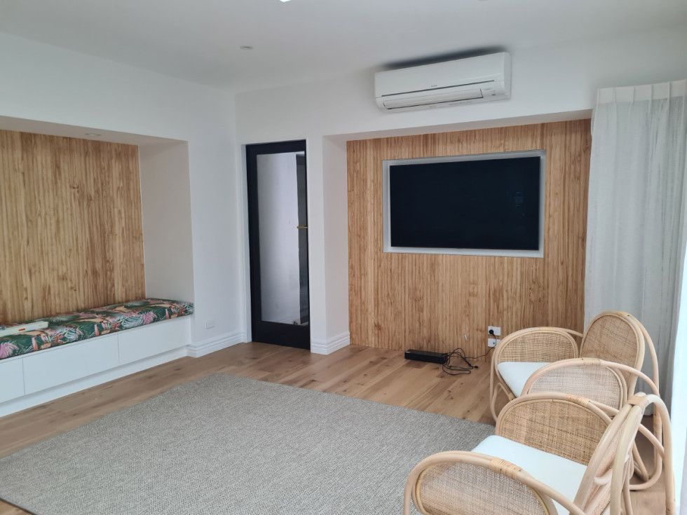 Living room with light wood paneling, TV, rattan chairs, and built-in bench.