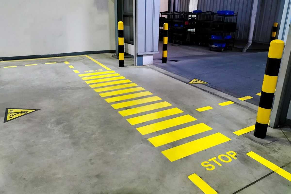 Yellow painted stop markings and pedestrian crossing on industrial concrete floor. Black and yellow safety bollards.