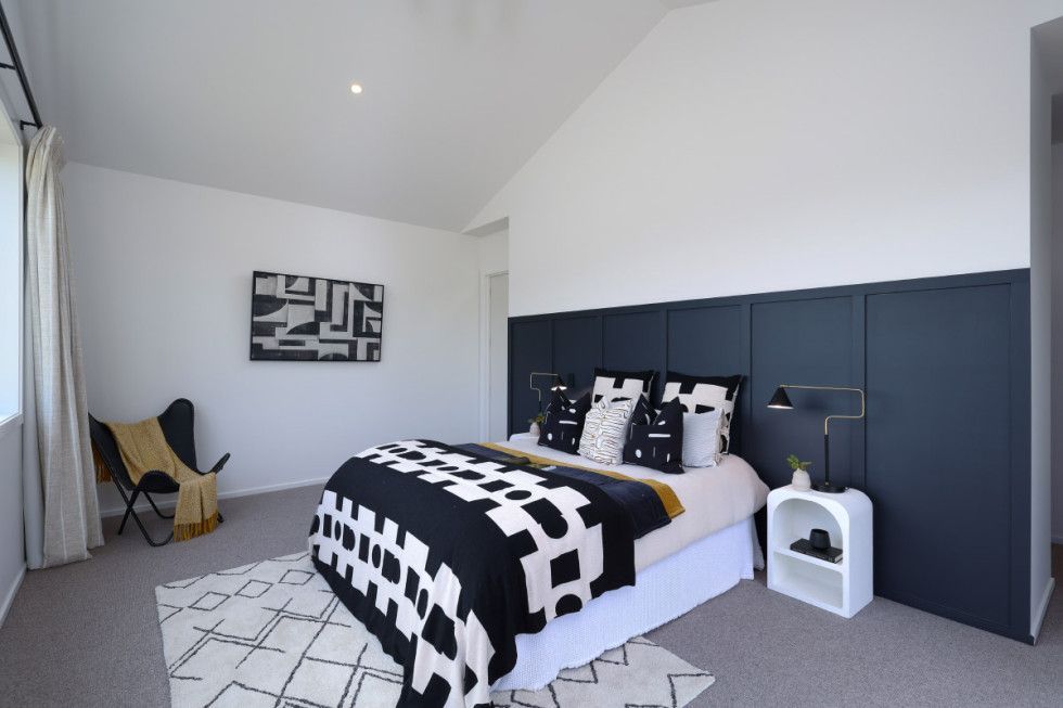 Bedroom with white walls, black and white bedding, art, and a dark blue panel behind the bed.