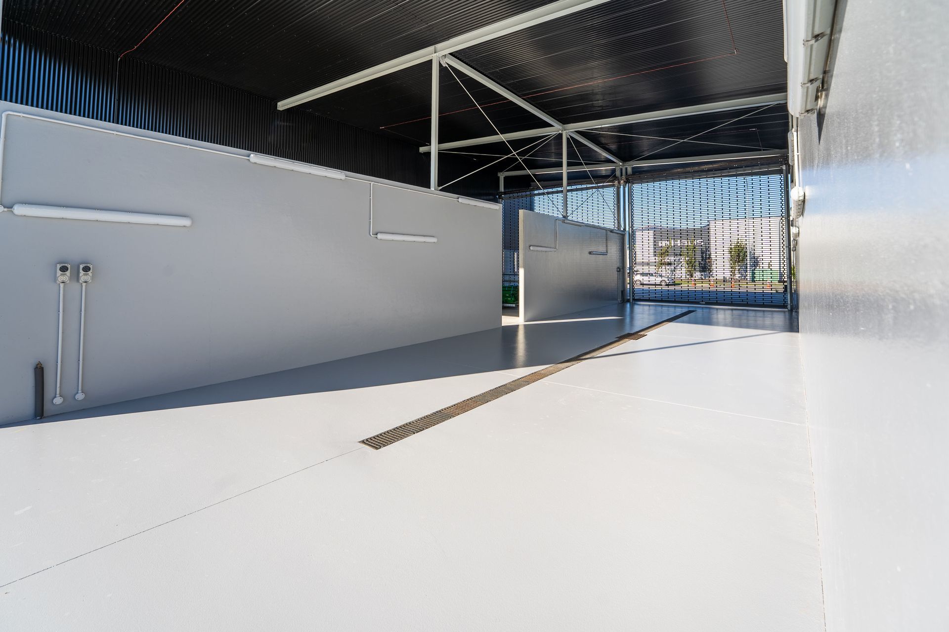 Interior of a metallic-walled structure with a light gray floor and walls, and black corrugated ceiling.