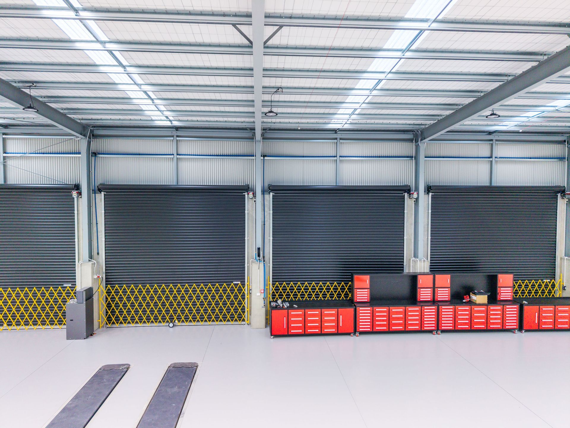 Interior view of a warehouse with roll-up doors, metal frame, and red tool cabinets.