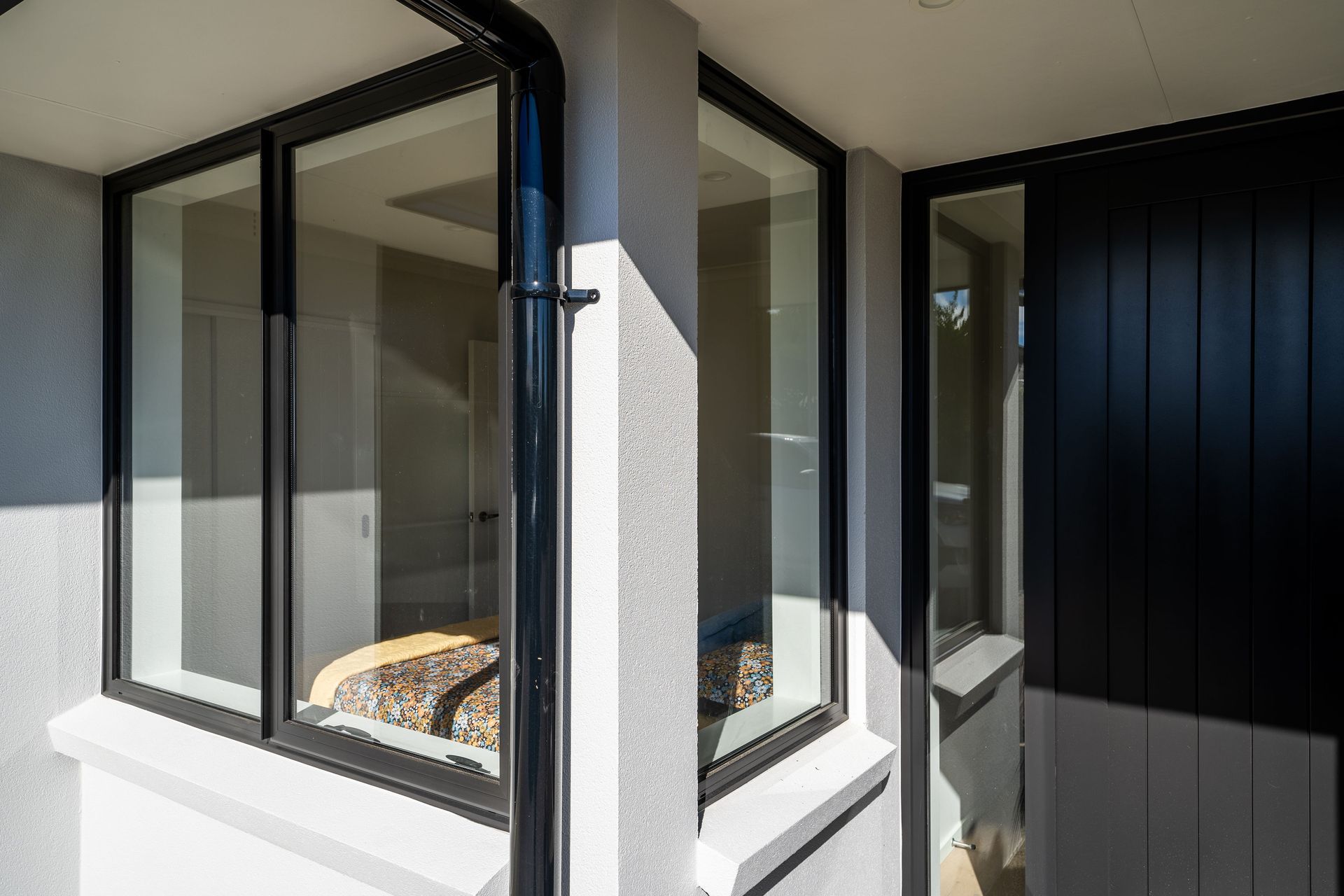 Black painted exterior wall with a window frame, window taped off, and gray spray paint residue.