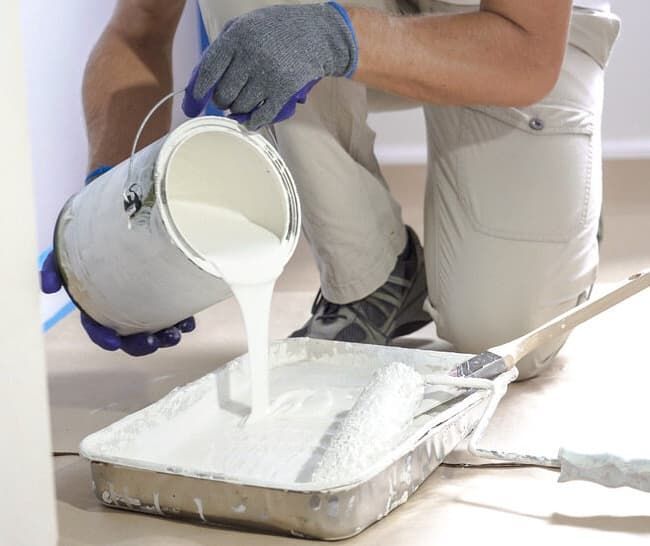 A Man Is Pouring White Paint Into a Tray — Greg Cannon Painting In Raymond Terrace, NSW