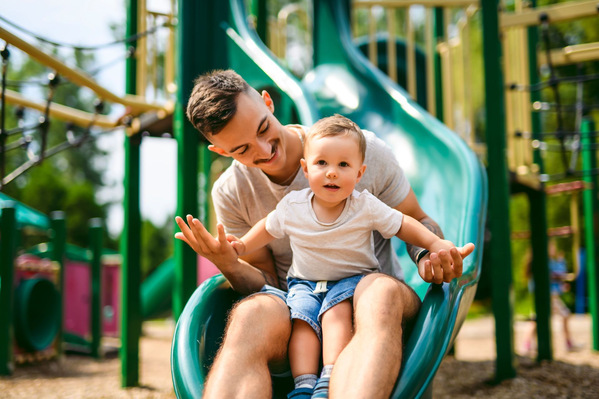 Man and child sliding down a green playground slide