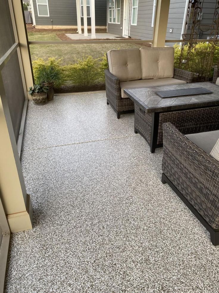 A patio with gray speckled flooring, wicker furniture, and a fire pit.