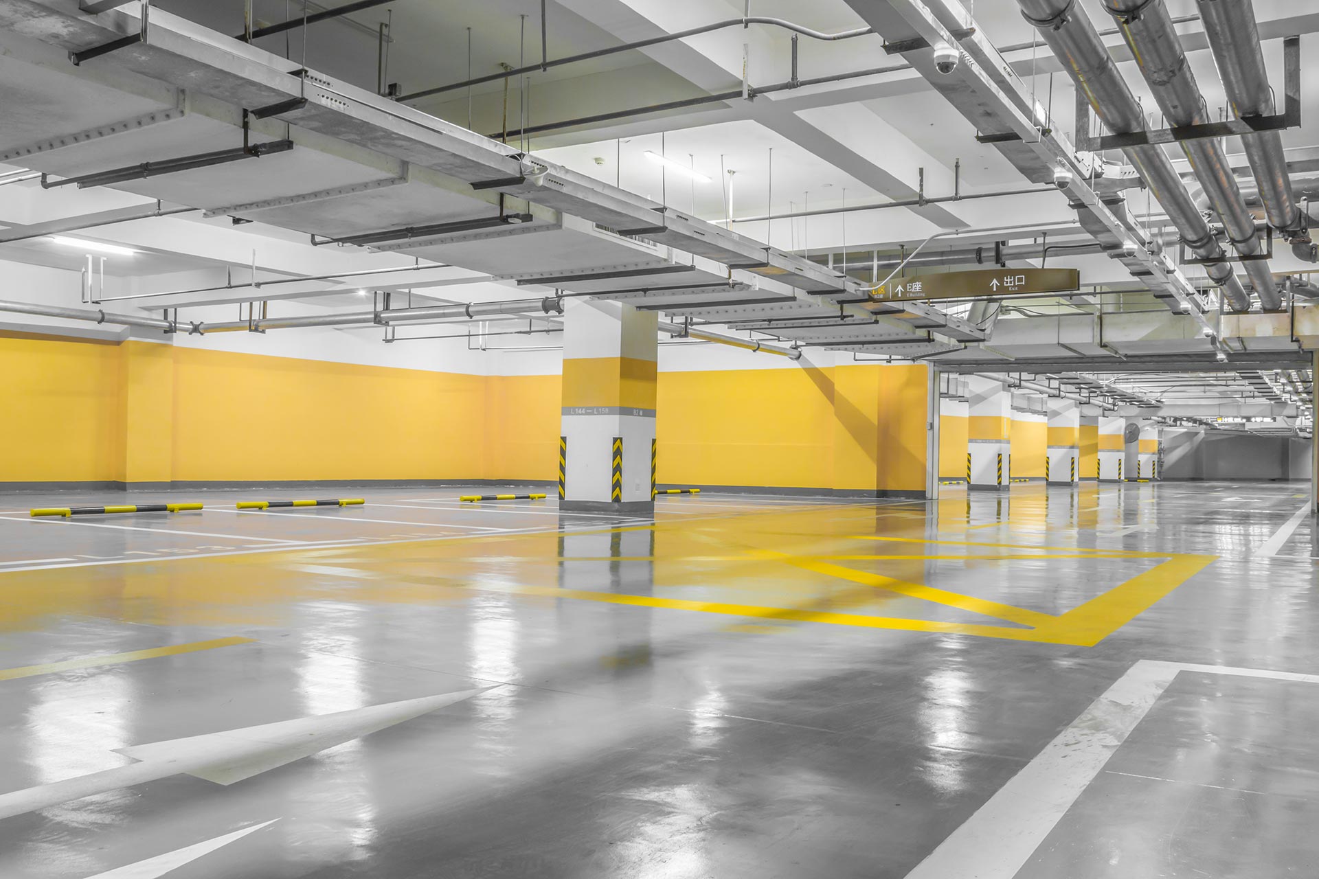 Brightly lit, empty parking garage with yellow walls and floor markings; gray floor and ceiling.