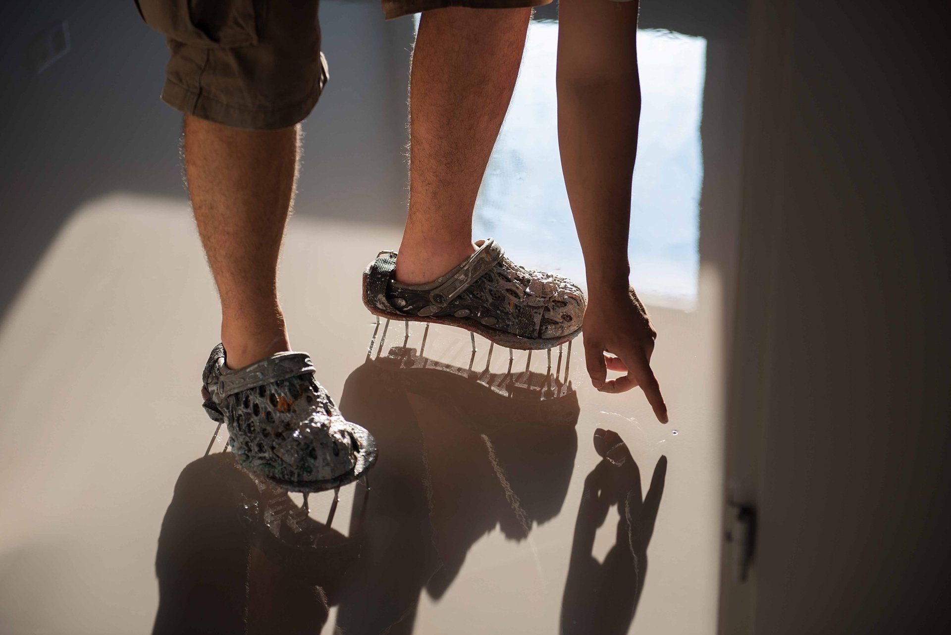 Person wearing shoes levitating, pointing at a shadow on the floor.