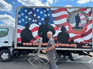 A man is carrying a chair in front of a truck that says veterans returning home