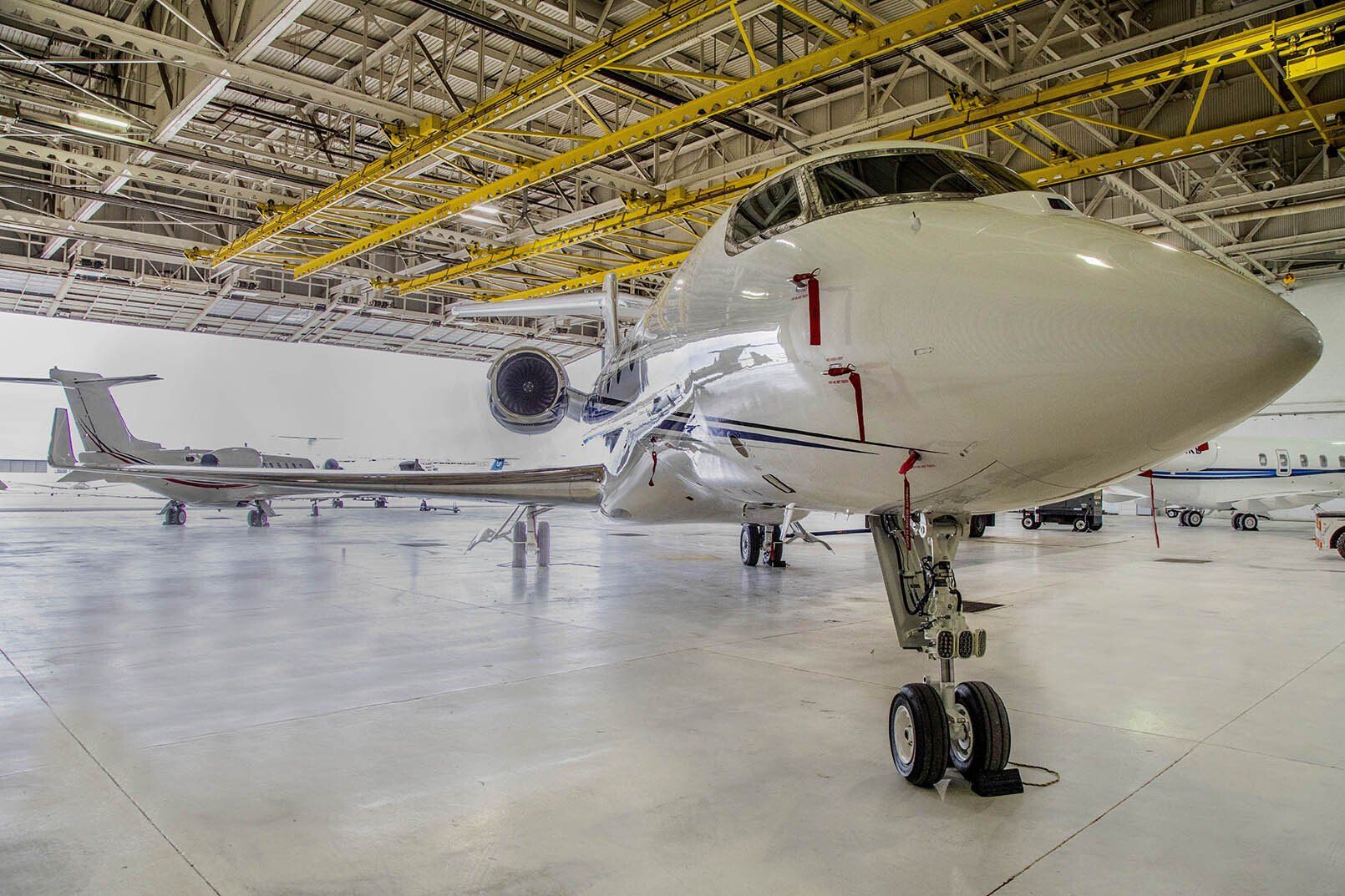 A white airplane is parked in a hangar with a yellow roof.