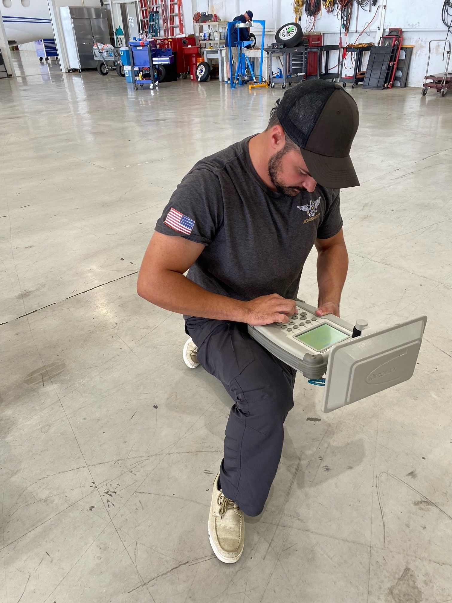 A man is kneeling down in a garage working on a computer.