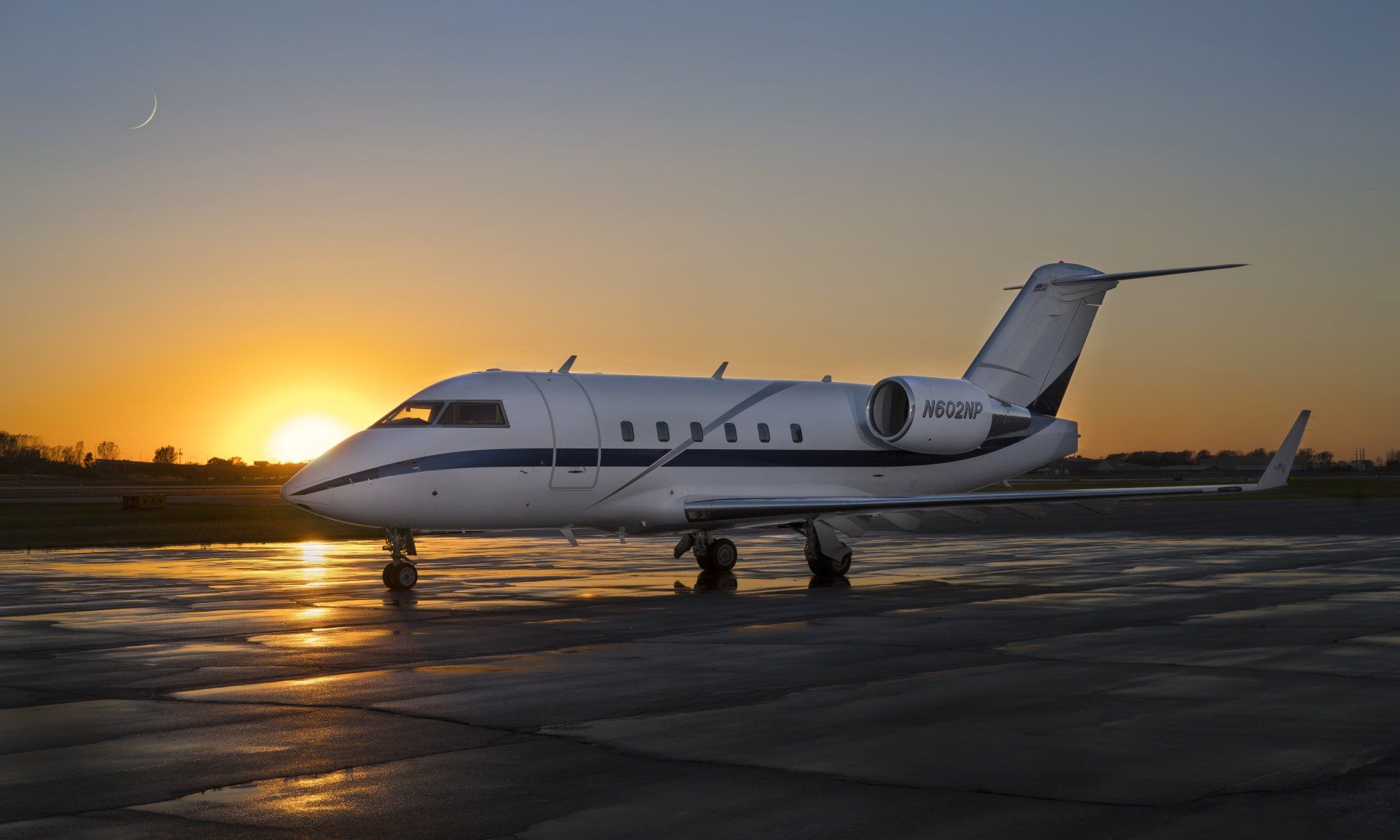 A small private jet is parked on the tarmac at sunset