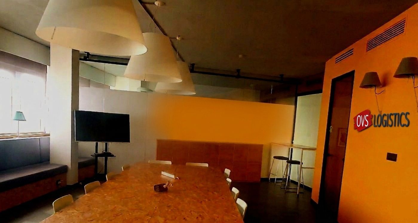 Orange-lit conference room with long table, wall-mounted TV, and a “Logistics” sign