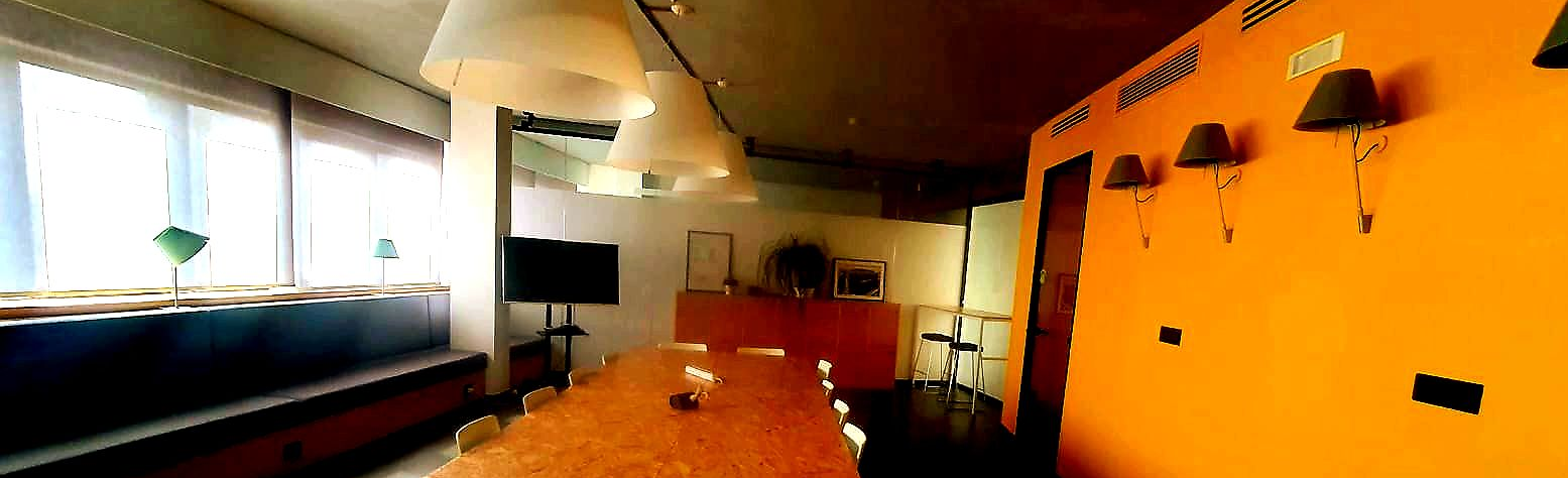 Long dining table in a room with orange wall, lamps, chairs, and window with natural light.