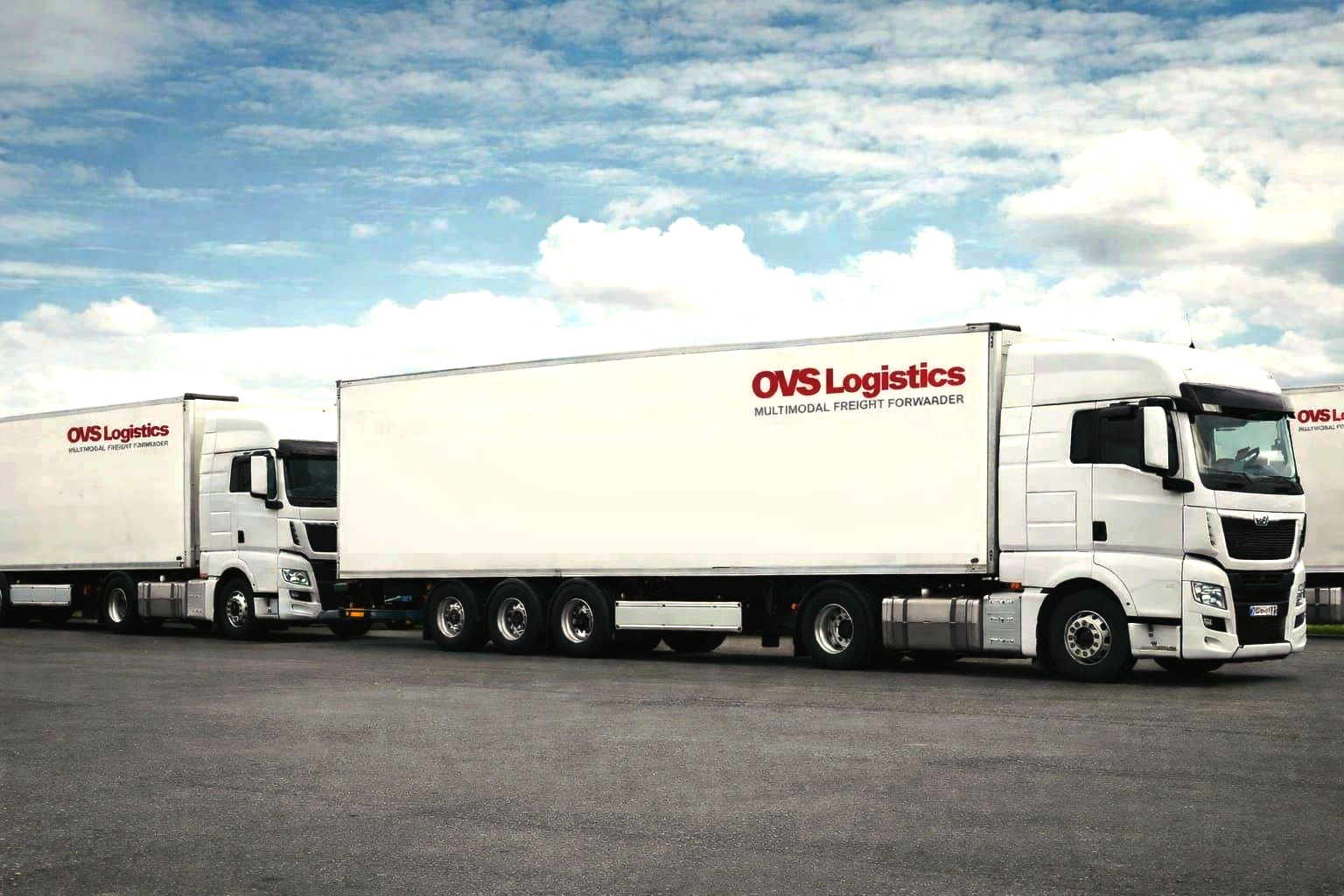 Freight train with shipping containers at a port, under blue sky, with cranes in background.