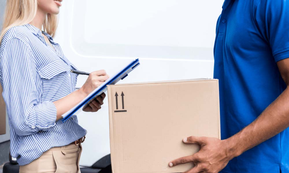 A delivery man is handing a box to a woman who is holding a clipboard.