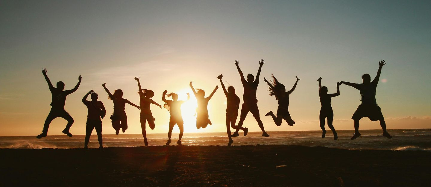 Silhouetted people jumping on a beach at sunset, arms raised.