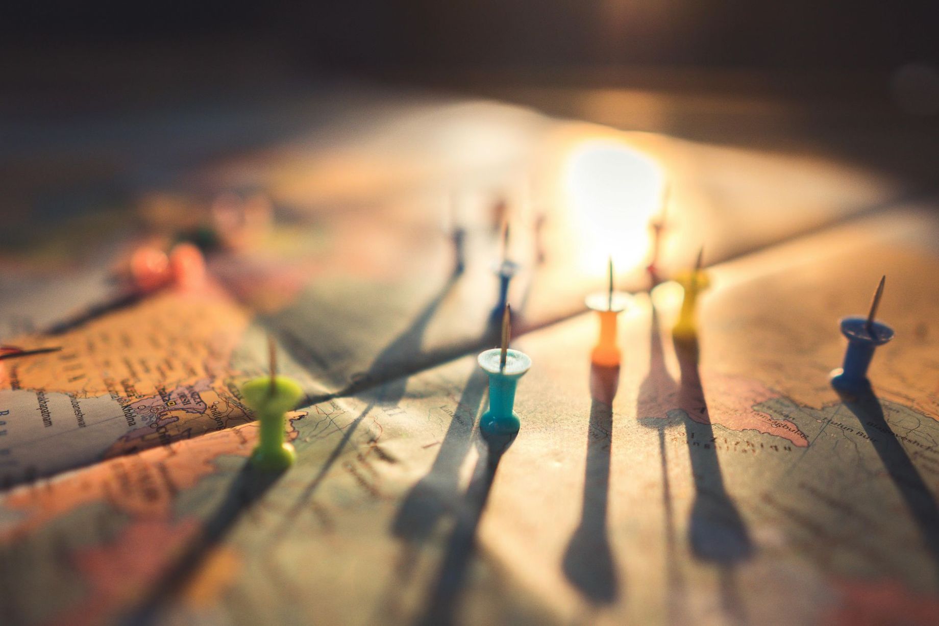 Colorful push pins on a map with warm sunlight and long shadows
