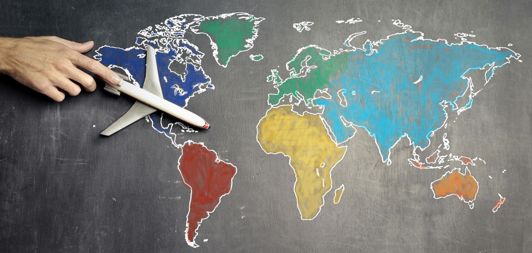 Hand holding toy airplane over a colorful chalk drawing of a world map.