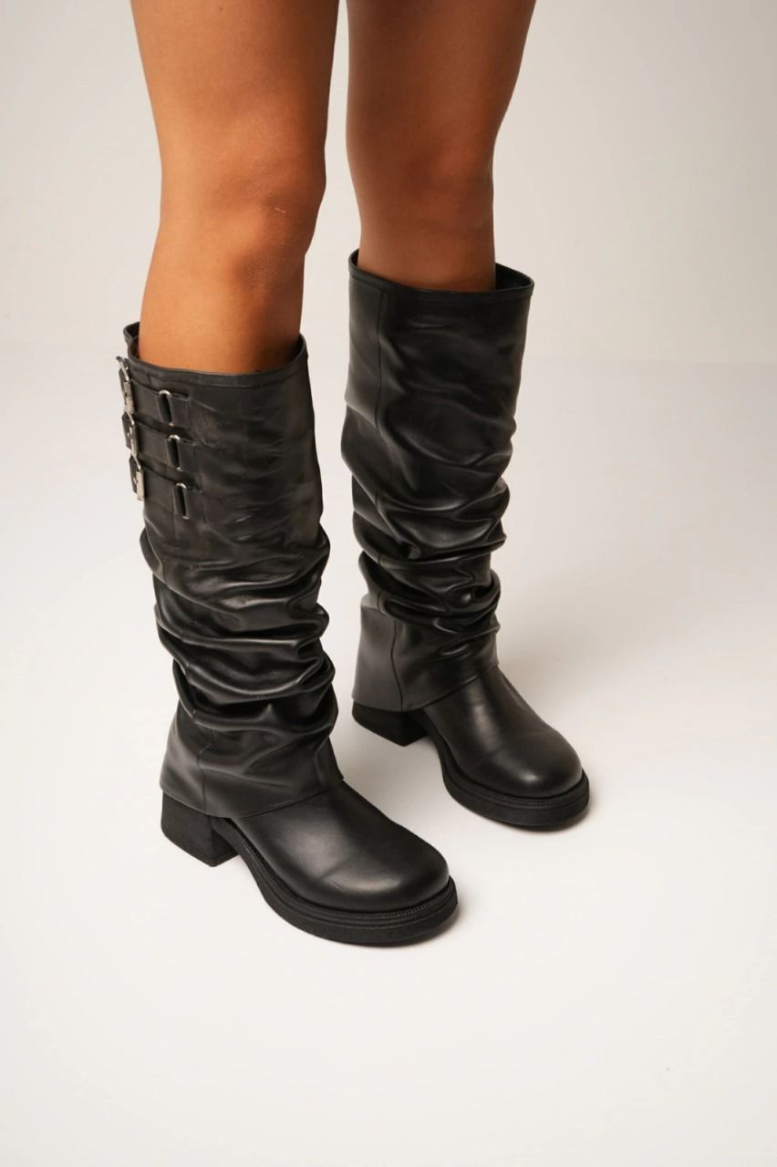 Mujer que lleva botas altas hasta la rodilla de cuero negro con detalles de hebillas.