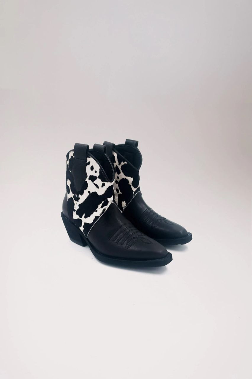 Un par de botas de vaquero con estampado de vaca en blanco y negro sobre un fondo blanco.