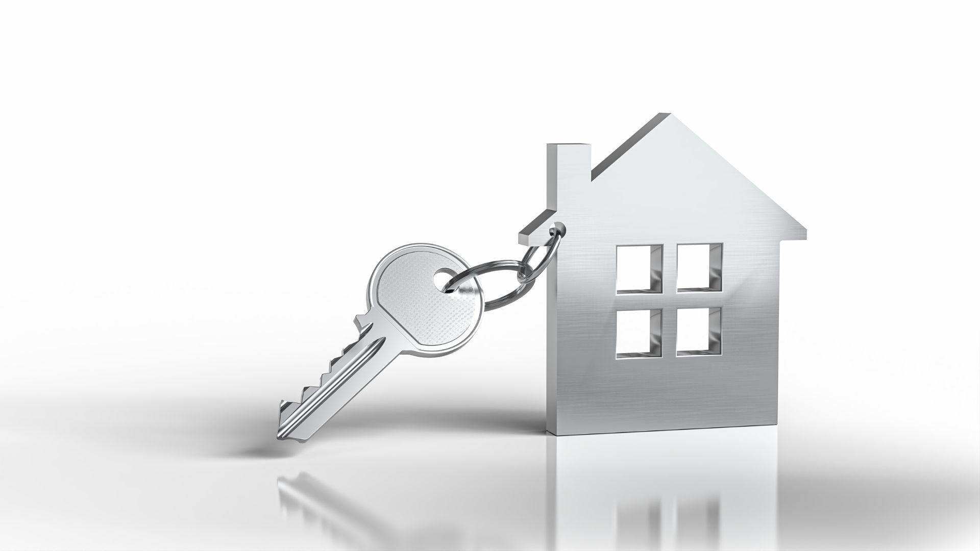 Silver house-shaped keychain with a metal key on a clean reflective surface, representing homeowners