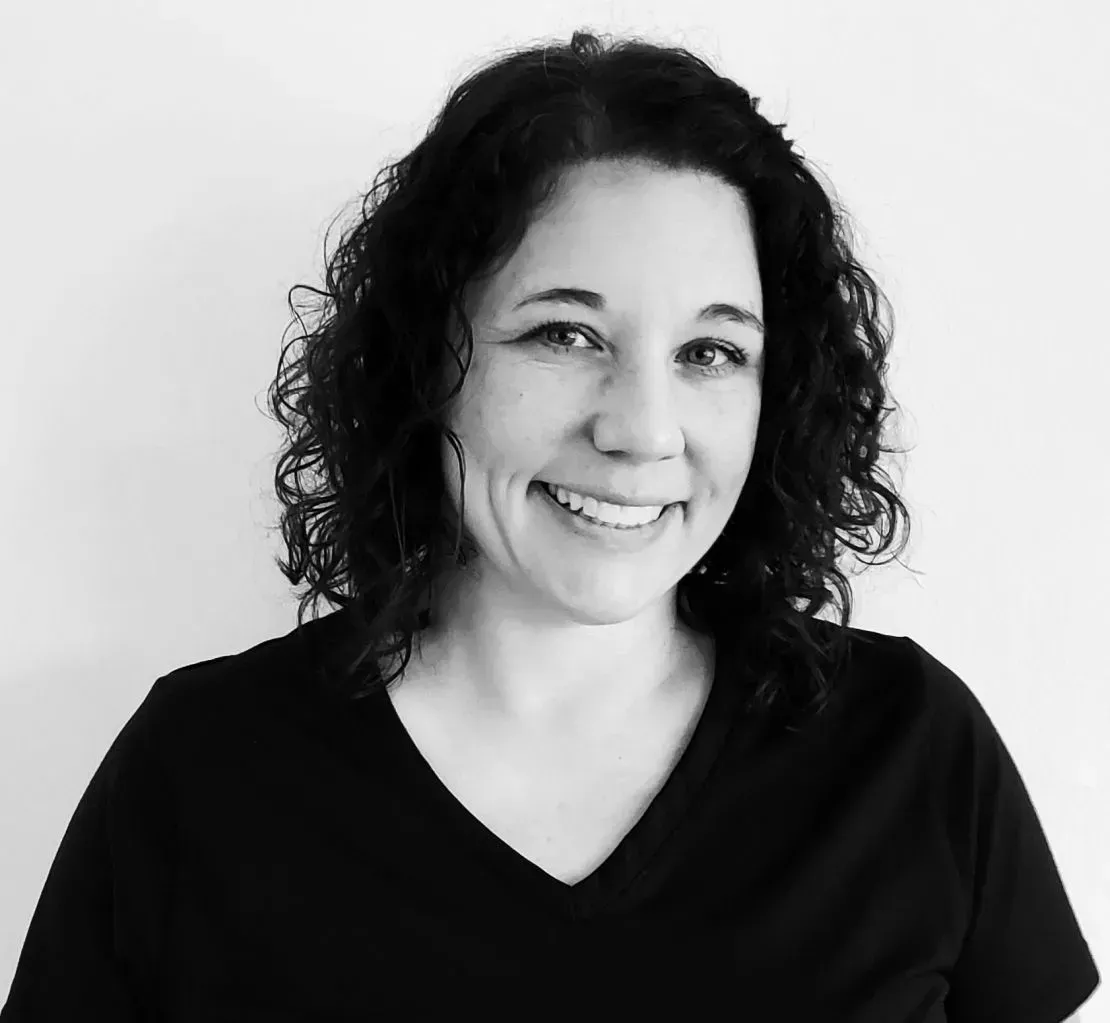 A woman with curly hair is smiling in a black and white photo.