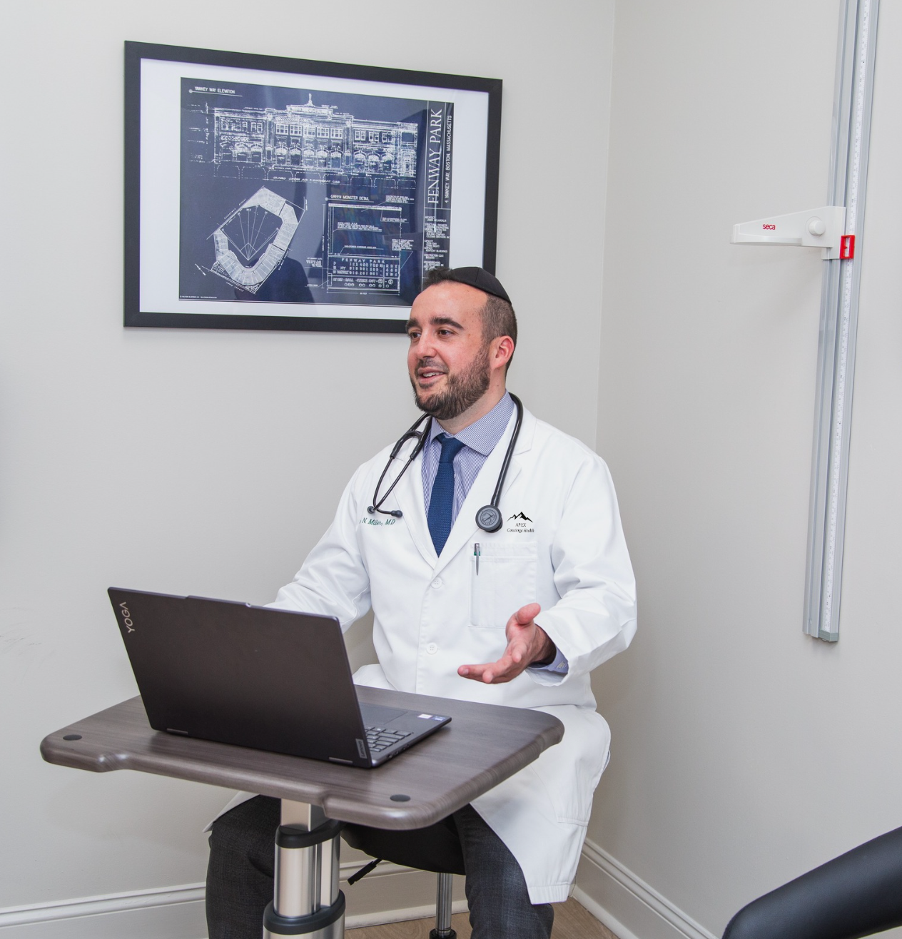 Doctor in white coat speaking beside a laptop in a clinic office
